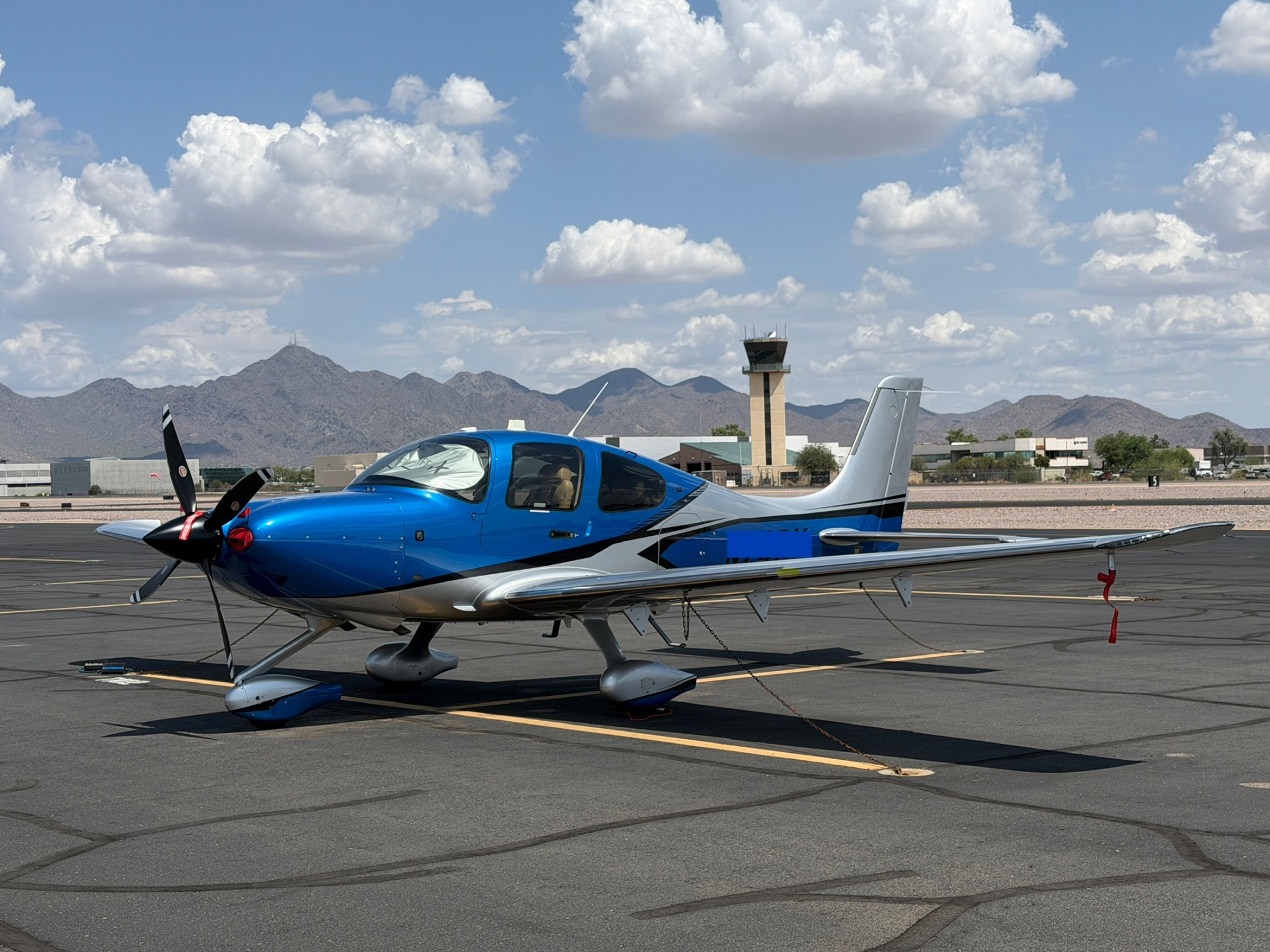 Blue Cirrus SR-series aircraft parked at a desert airport with mountains beyond